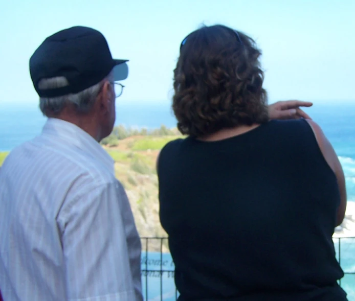 two people stand at a fence, with the ocean in the background