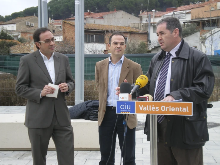 three men standing at a street sign with a microphone