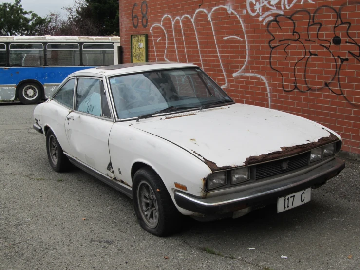 an old rusted car sits in front of some graffiti