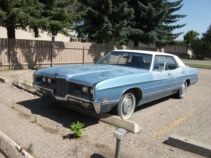 an old blue and white car sitting in the middle of the road