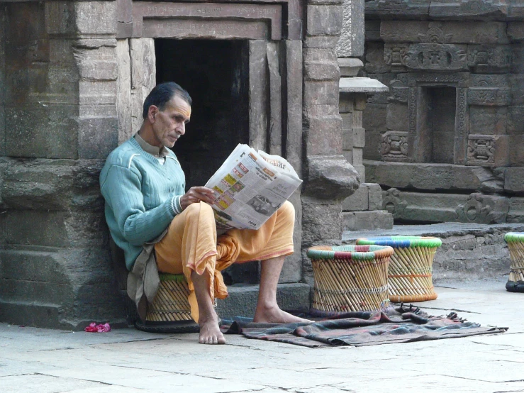 the man sits outside a cave house reading a paper