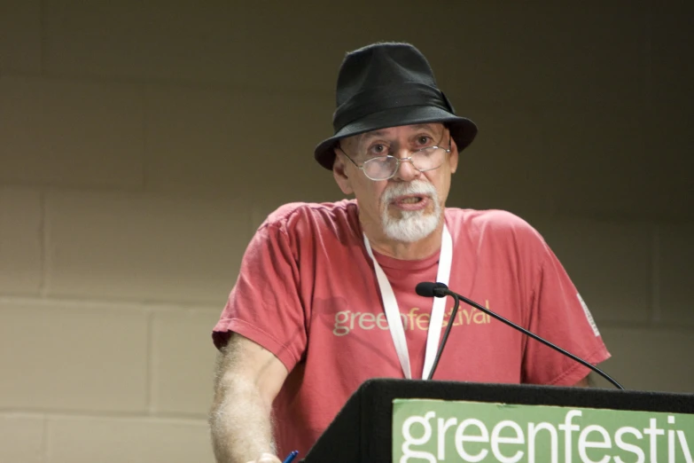 a man wearing glasses and a hat giving a speech