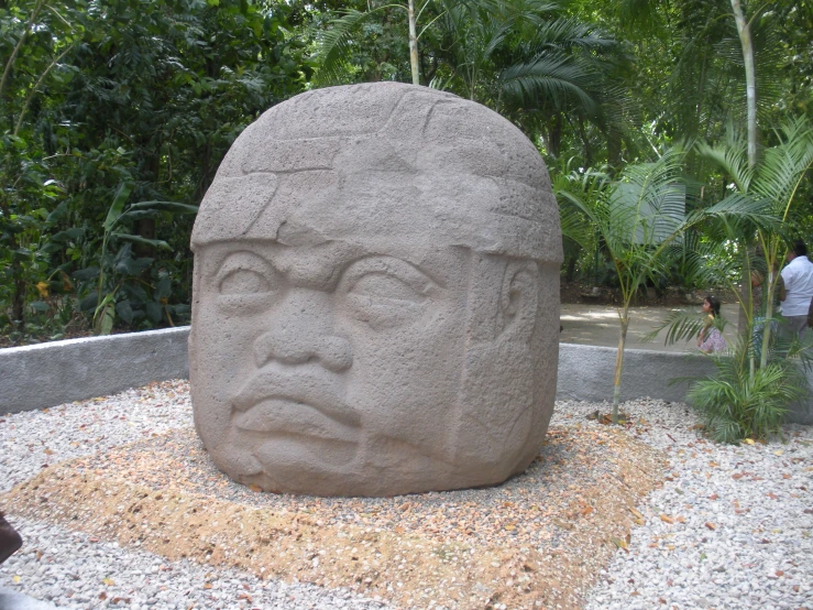 a cement statue of a face sitting on some gravel