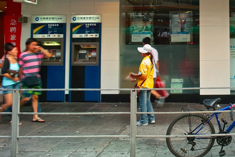 several people are walking by the atm on the sidewalk