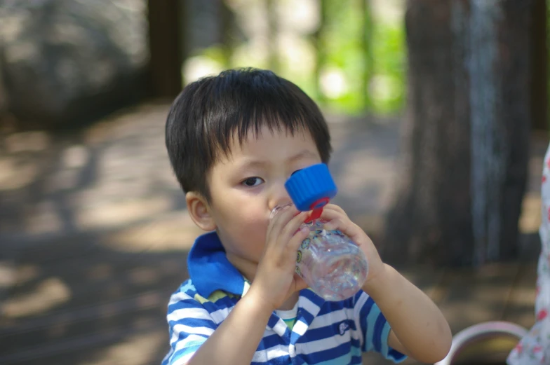 a child drinking from a bottle while standing in the woods