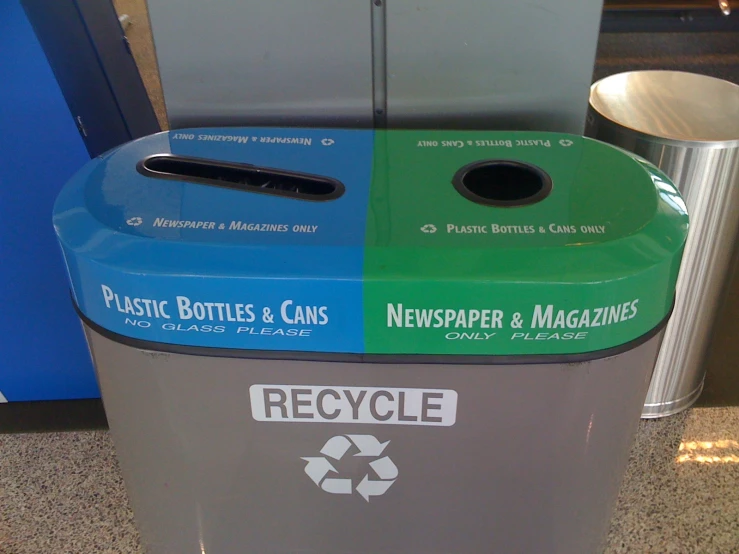 a green and grey recycle bin with two rolls of news paper