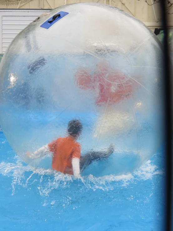 a boy plays inside a bubble ball in an enclosed pool