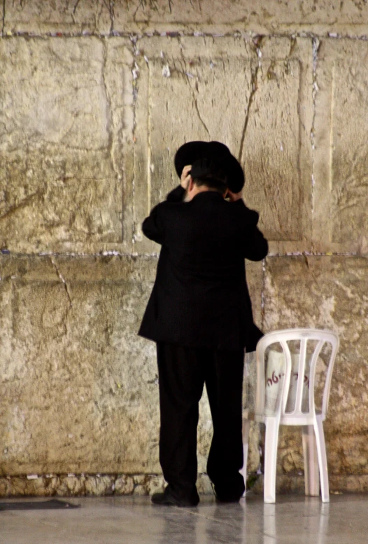 a person wearing a black suit and hat while standing near a chair