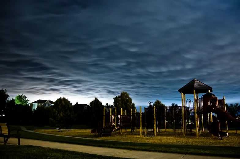 an empty playground sits in the middle of a field with a cloudy sky