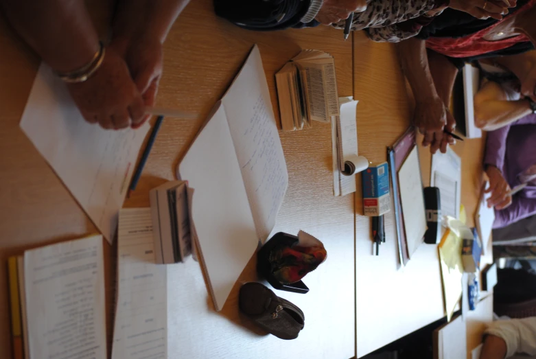 group of people sitting at a table using different sized pens