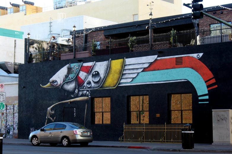 a car passes by a very colorful wall with buildings in the background