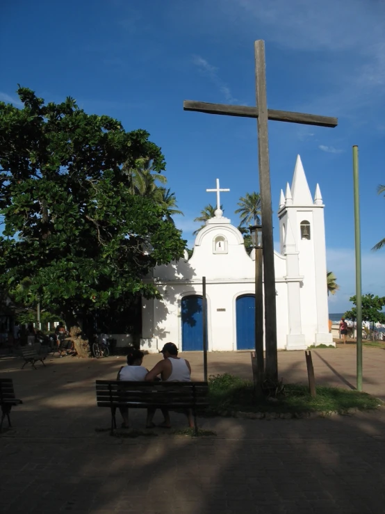there is a man and a woman sitting on a bench near a cross