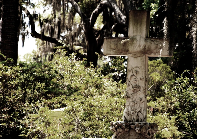 an old stone cross stands in the grass by trees