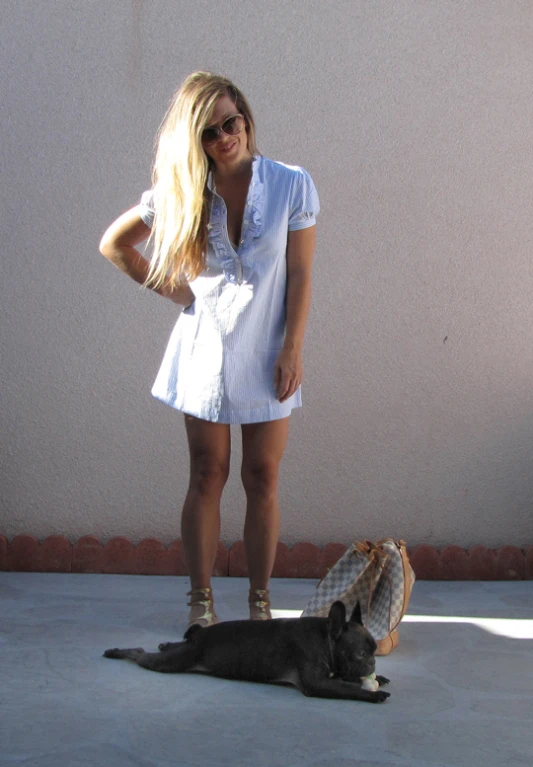 a woman in a short dress posing next to a dog on concrete