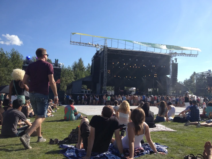 an outdoor concert stage with many people sitting and standing in the grass