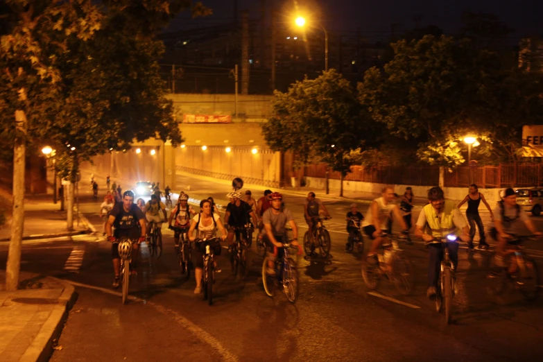 a group of bicyclists on bicycles riding through the street at night