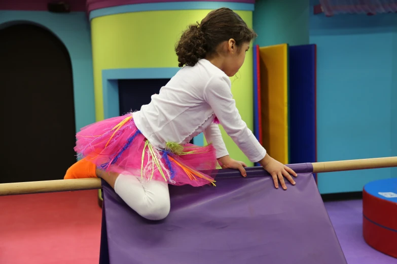 a little girl in white shirt and pink skirt standing on a purple fence