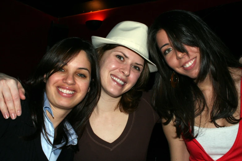 three women wearing hats pose for a po