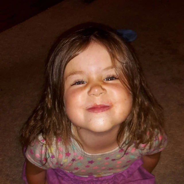 a young child smiles while sitting on the ground