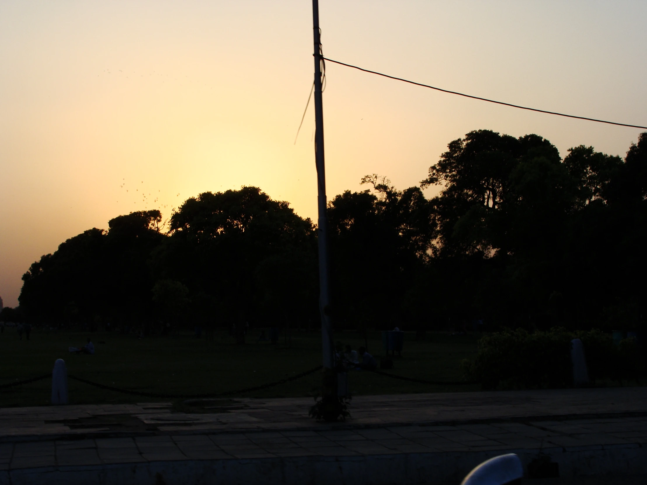 the sun is setting in a park that has some trees