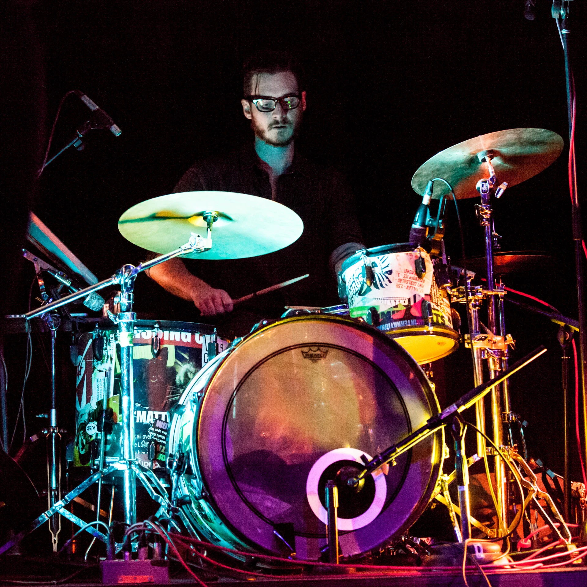 a drummer is playing drums in front of bright colored lights