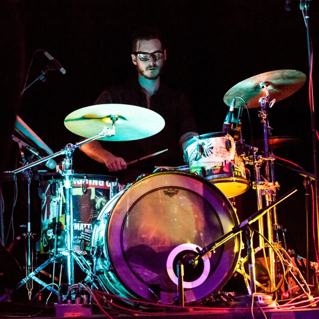 a drummer is playing drums in front of bright colored lights