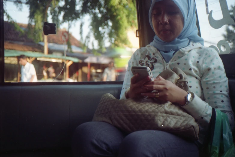 a women sitting on a bus holding her cell phone