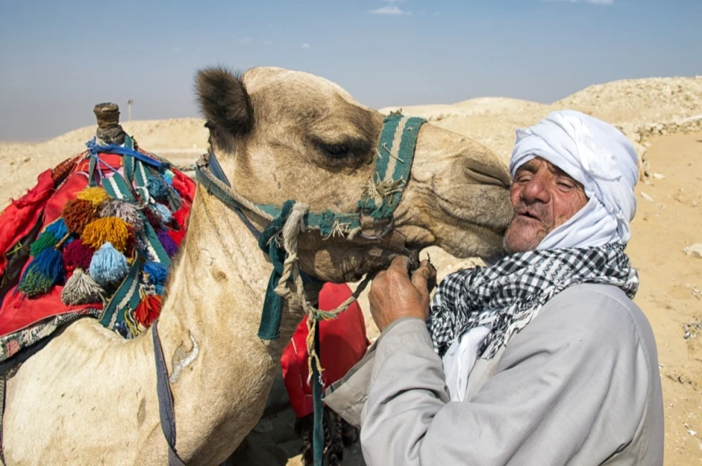 a man wearing a head scarf and sitting on a camel