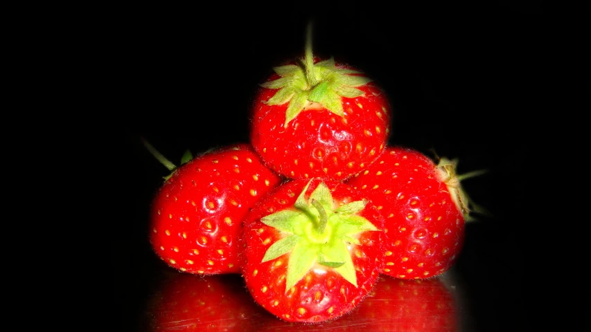 four ripe strawberries are piled on top of each other