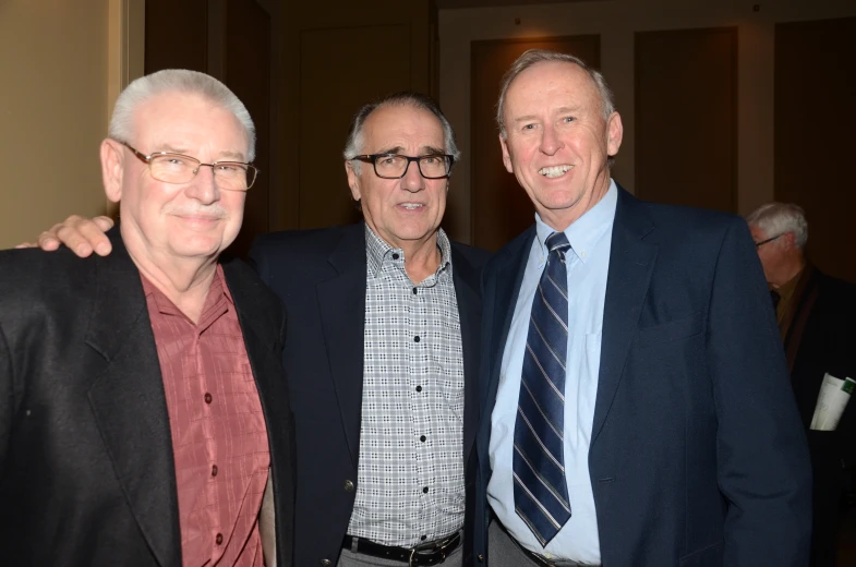 two men are posing with another man in a suit