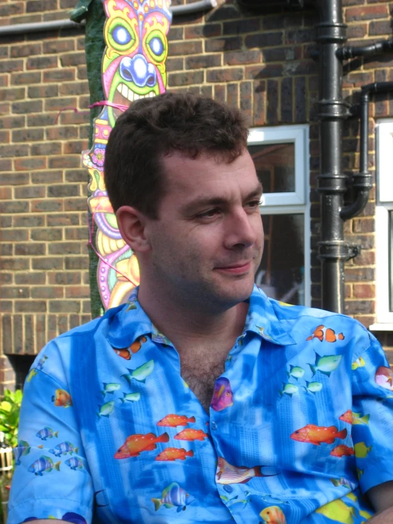 man in blue hawaiian shirt sitting outdoors with colorful mural on wall