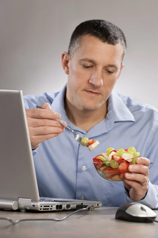 a man sitting in front of a laptop and eating food