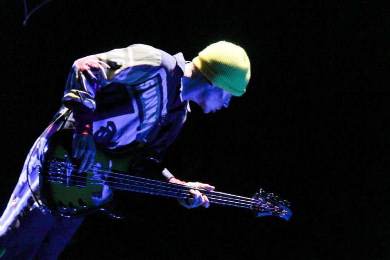 a man wearing blue and white outfit playing bass in black background