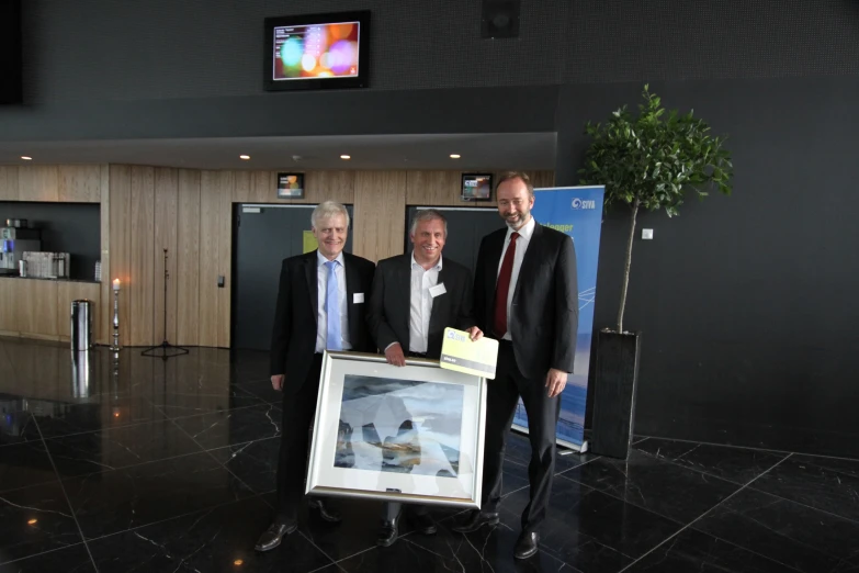 three men pose for the camera while one holds a large picture in his hands