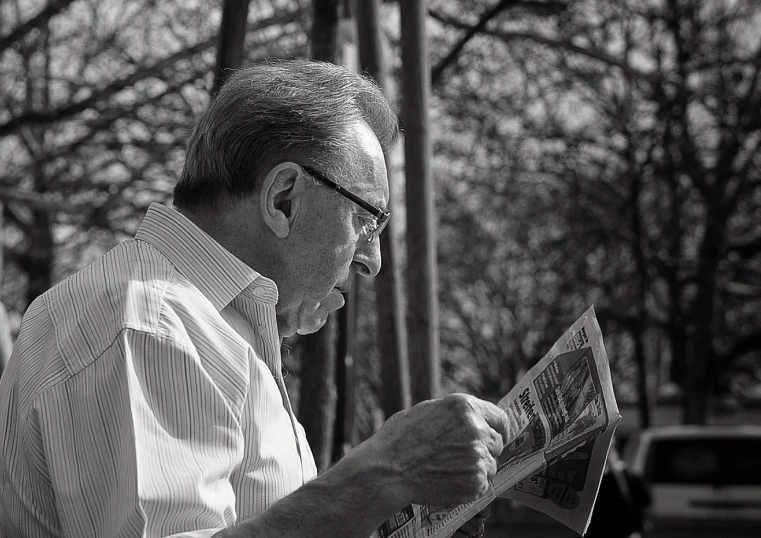 a man reading a newspaper while standing next to a tree