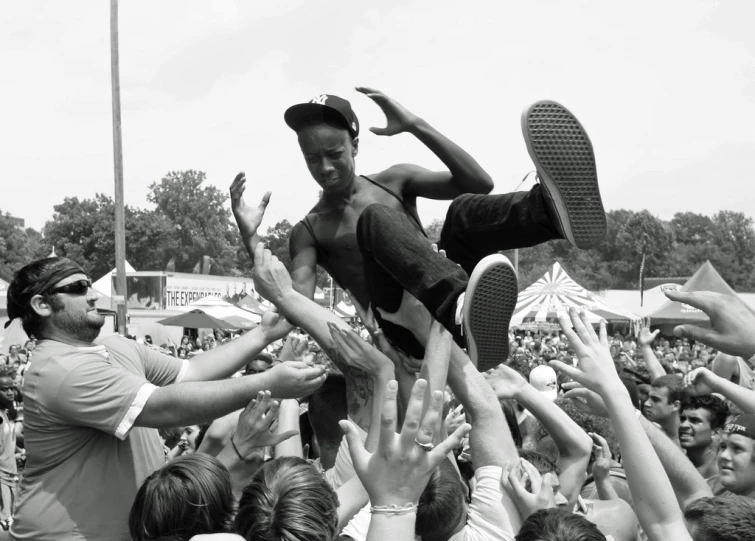 man in hat holding up foot above hands while people hold him