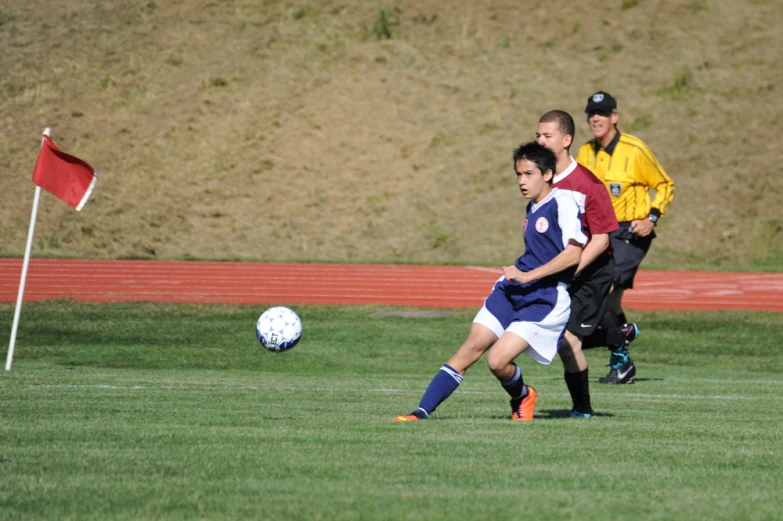 two men playing soccer in the grass with a referee watching