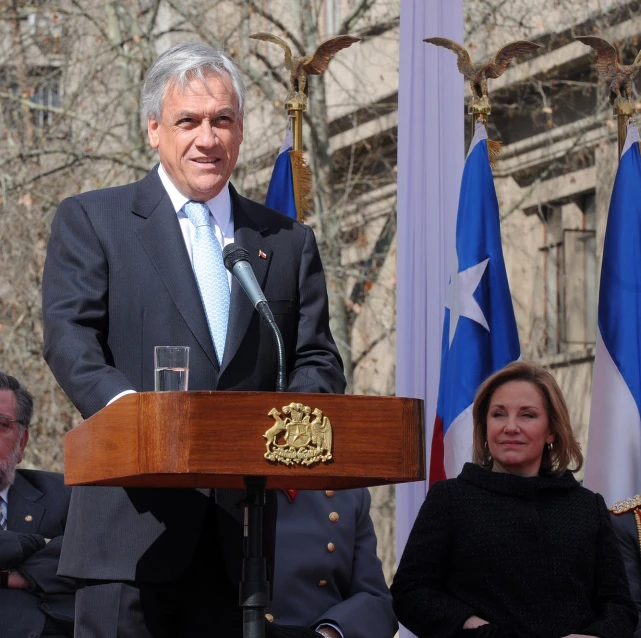 a man speaking at a podium next to flags