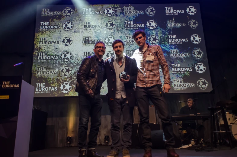 three men standing on stage with microphones in front of them