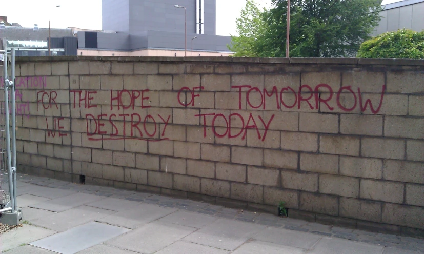 writing spray painted on a stone wall saying stop the type of tomorrow we destroy today