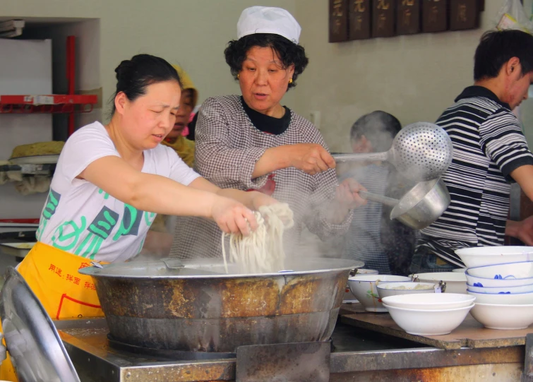 two women and an asian man working in a cooking school