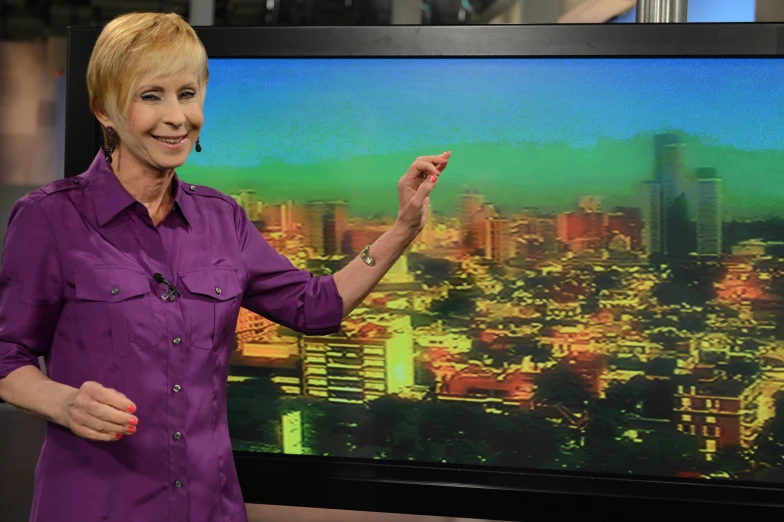 an older woman pointing towards a cityscape on the tv