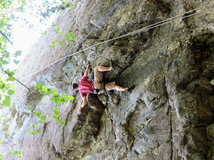 man climbing up a large rock next to a forest