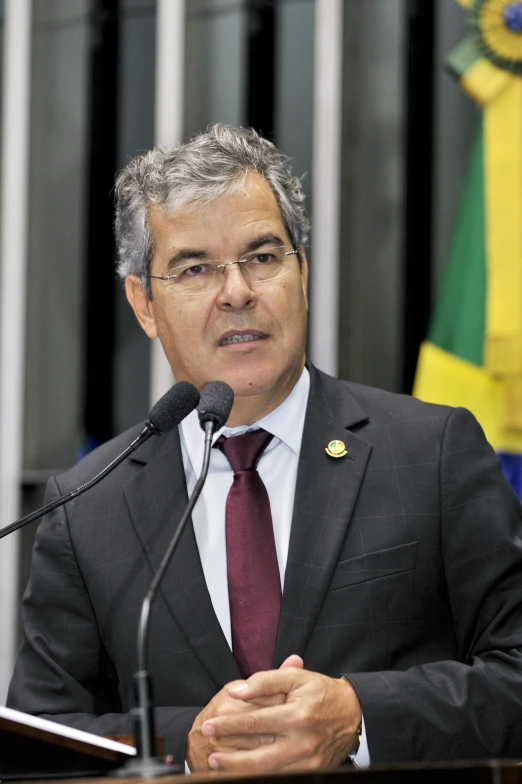 a man in a business suit and tie sits behind a microphone at a press conference