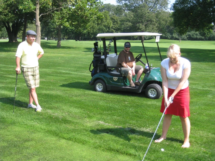 a woman is holding a golf club by her foot while another man is on a golf cart behind her