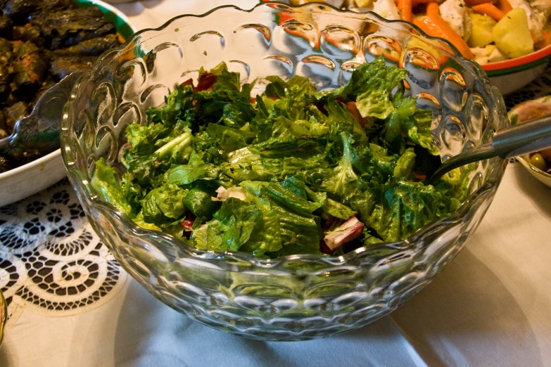 a glass bowl is filled with salad on a table