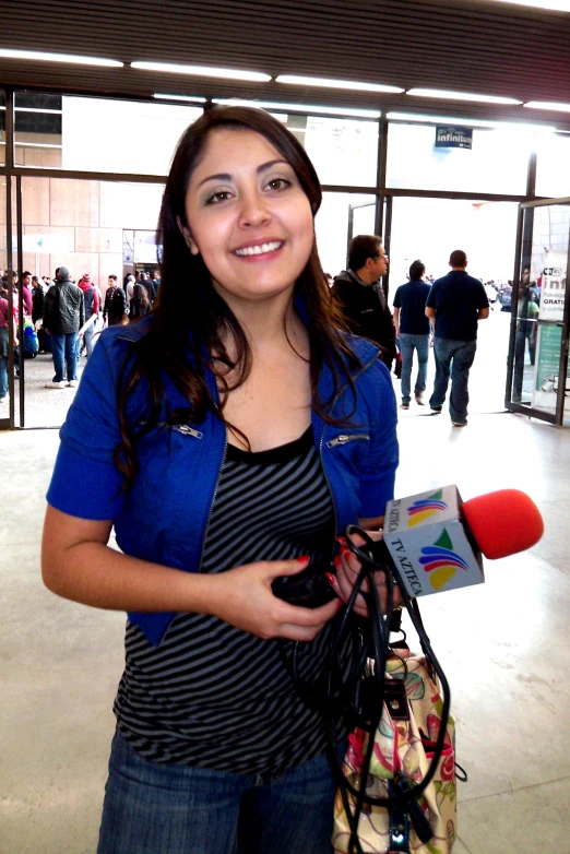 woman in striped shirt holding camera with microphone at indoor event