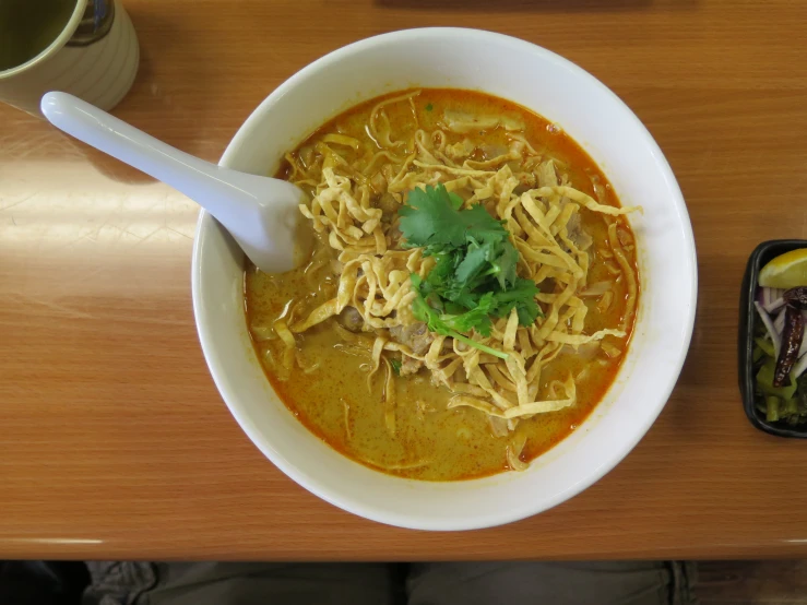 a bowl of soup with noodles and cilantro on the side