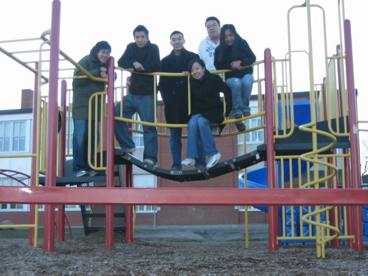 four people are posing on a red and yellow play structure