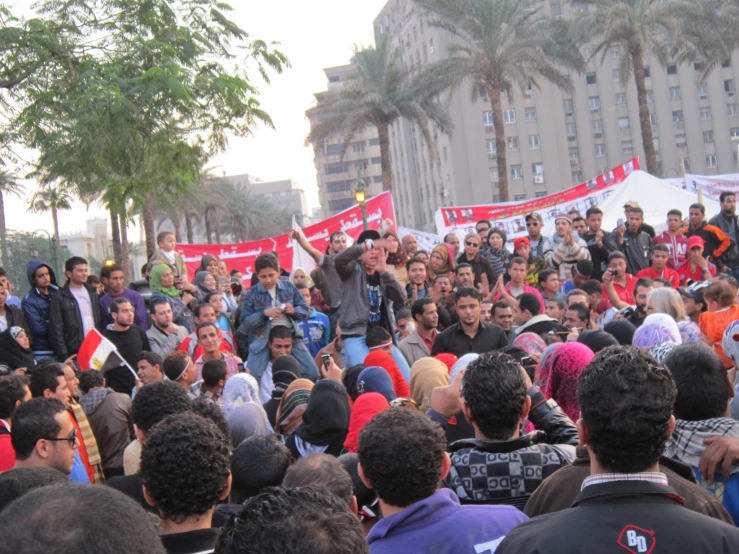 several men stand in front of a crowd with signs and flags